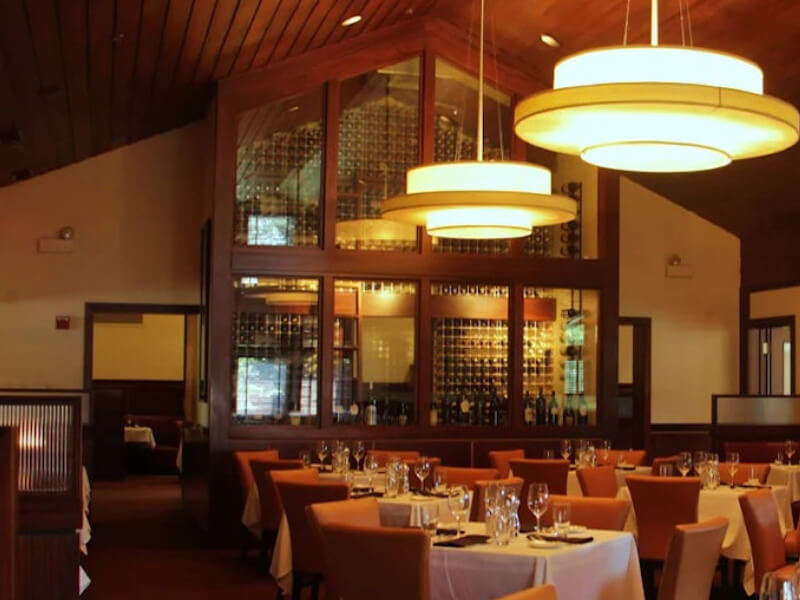 Floor-to-ceiling wine rack wall with polished aluminum framing behind leather booth seating at a steakhouse in Lincolnshire, Illinois