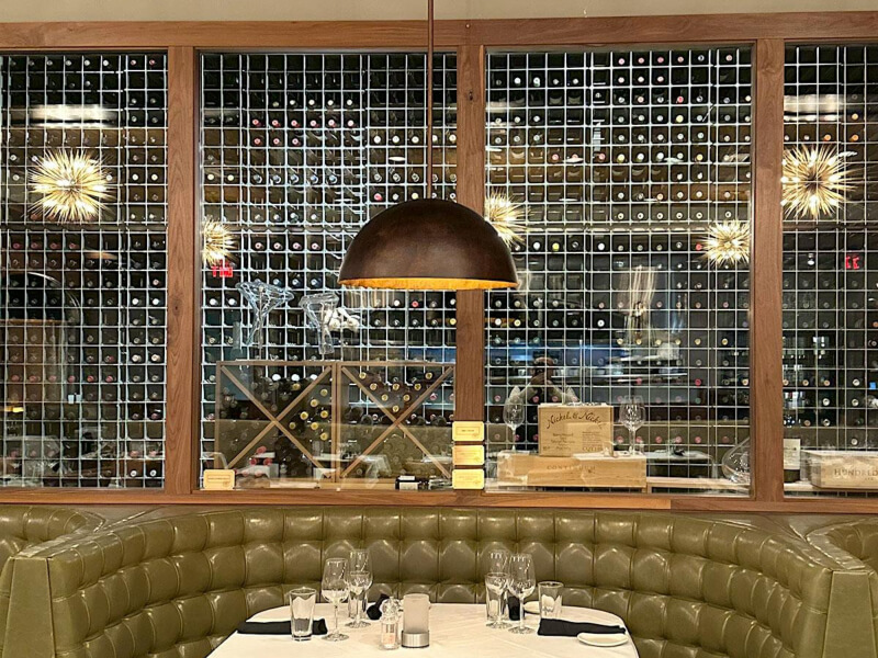 Guests dining beneath a floor-to-ceiling wine wall with aluminum framing and professional lighting at a  steakhouse in Naperville, Illinois