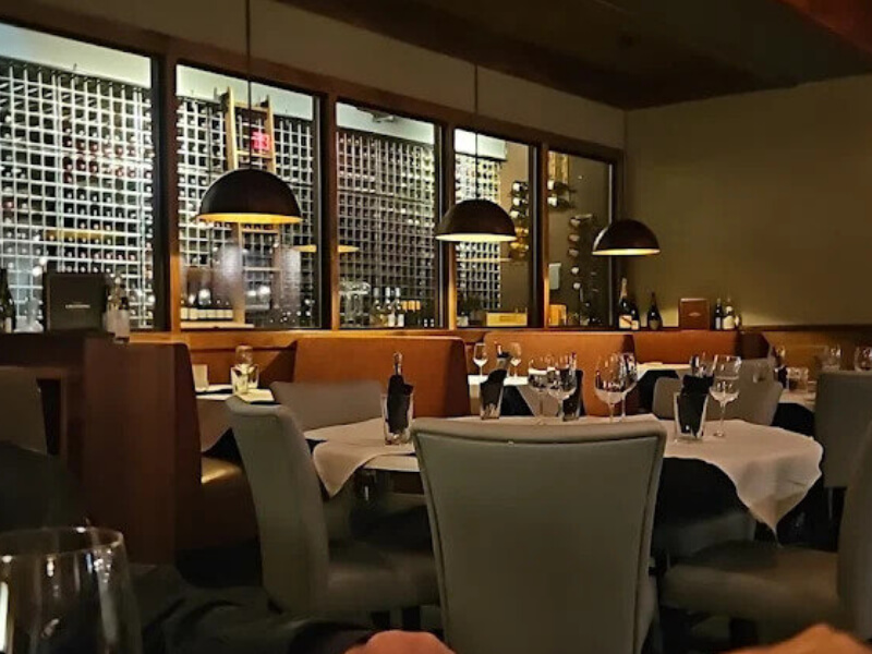 Wide view of fine dining room with floor-to-ceiling wine wall behind booth seating at a steakhouse in  Delaware