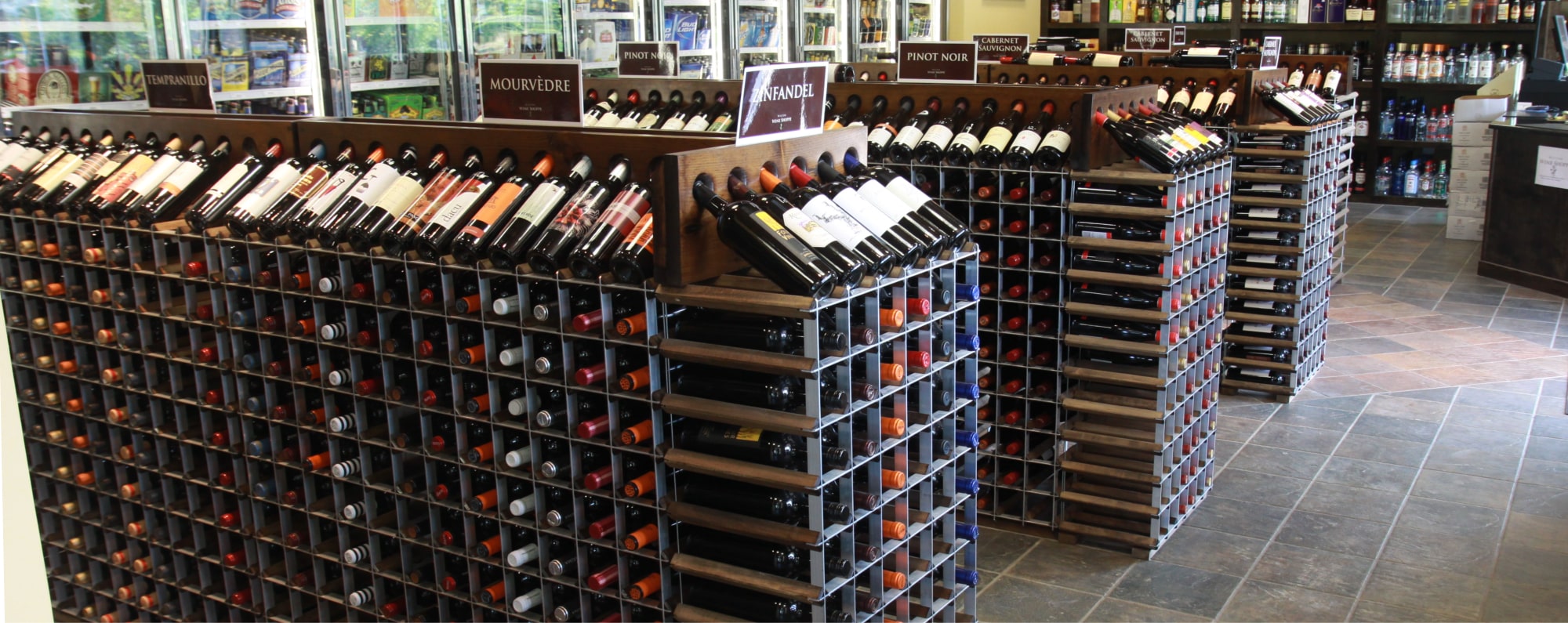 A retail store displaying an array of wine rack options, including wall racks, two-sided aisle racks, and end caps at the end of each aisle
